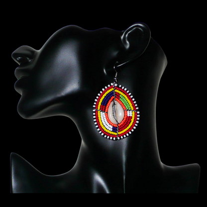 Boucles d'oreilles africaines à motifs ethniques composées de perles et de coquillages montés en forme de boucliers Massai. Elles mesurent 7 cm de long et 4 cm de large et se portent sur des oreilles percées. 