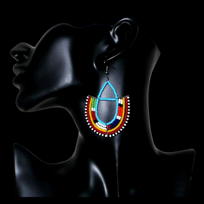 Boucles d'oreilles ethniques Massai bleues et multicolores en perles de rocaille montées en forme d'ancres. Elles mesurent 7.5 cm de long et se portent sur des oreilles percées.
