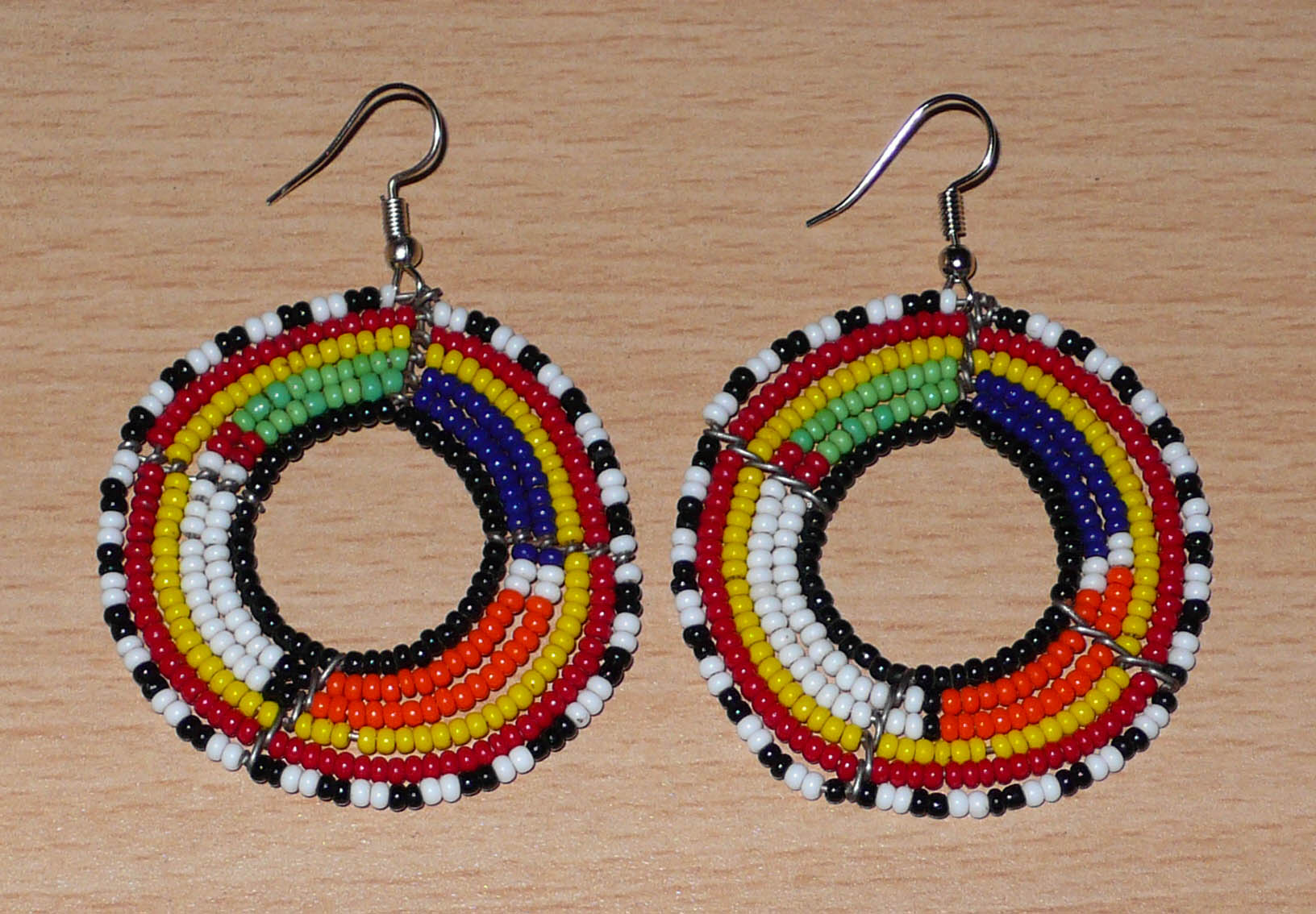 Boucles d'oreilles africaines perlées se composant de perles de rocaille enfilées sur des structures circulaires faites de six rangées de fils de fer. Elles mesurent 7 cm de long et 5 cm de large et se portent avec des crochets en acier inoxydable.