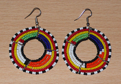 Boucles d'oreilles africaines perlées se composant de perles de rocaille enfilées sur des structures circulaires faites de six rangées de fils de fer. Elles mesurent 7 cm de long et 5 cm de large et se portent avec des crochets en acier inoxydable.