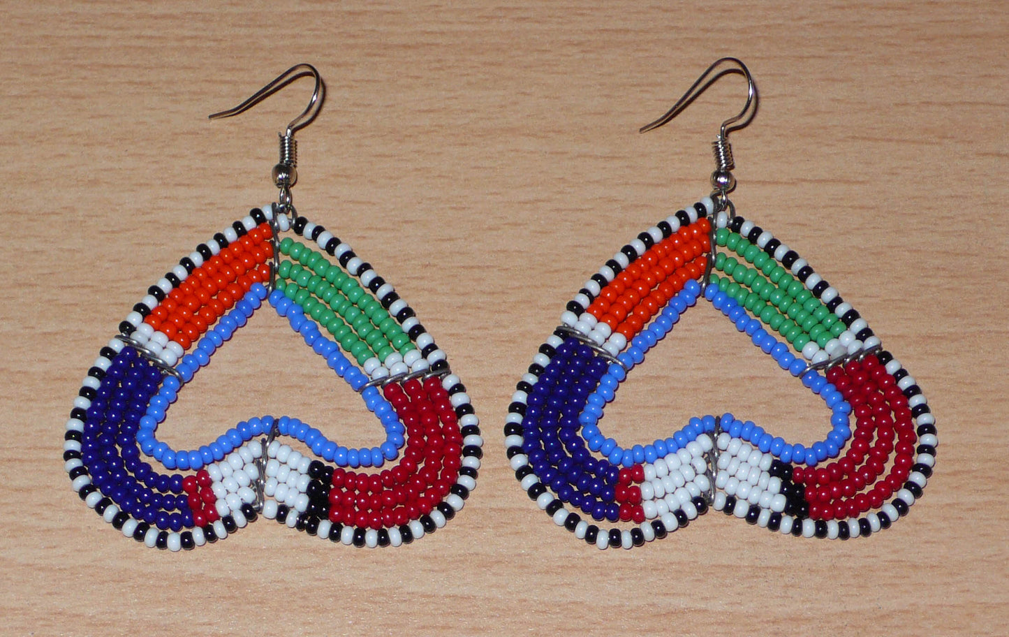 Boucles d'oreilles africaines kenyanes de fabrication artisanale Massai composées de perles de rocaille multicolores glissées sur cinq rangées de fils de fer montés en forme de cœurs inversés. Cette paire de boucles d'oreilles de taille moyenne mesure 6.5 cm de long et 5 cm de large ; elle se porte avec des crochets en acier inoxydable sur des oreilles percées.