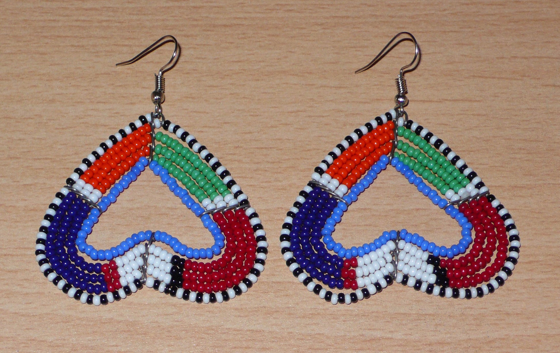 Boucles d'oreilles africaines kenyanes de fabrication artisanale Massai composées de perles de rocaille multicolores glissées sur cinq rangées de fils de fer montés en forme de cœurs inversés. Cette paire de boucles d'oreilles de taille moyenne mesure 6.5 cm de long et 5 cm de large ; elle se porte avec des crochets en acier inoxydable sur des oreilles percées.