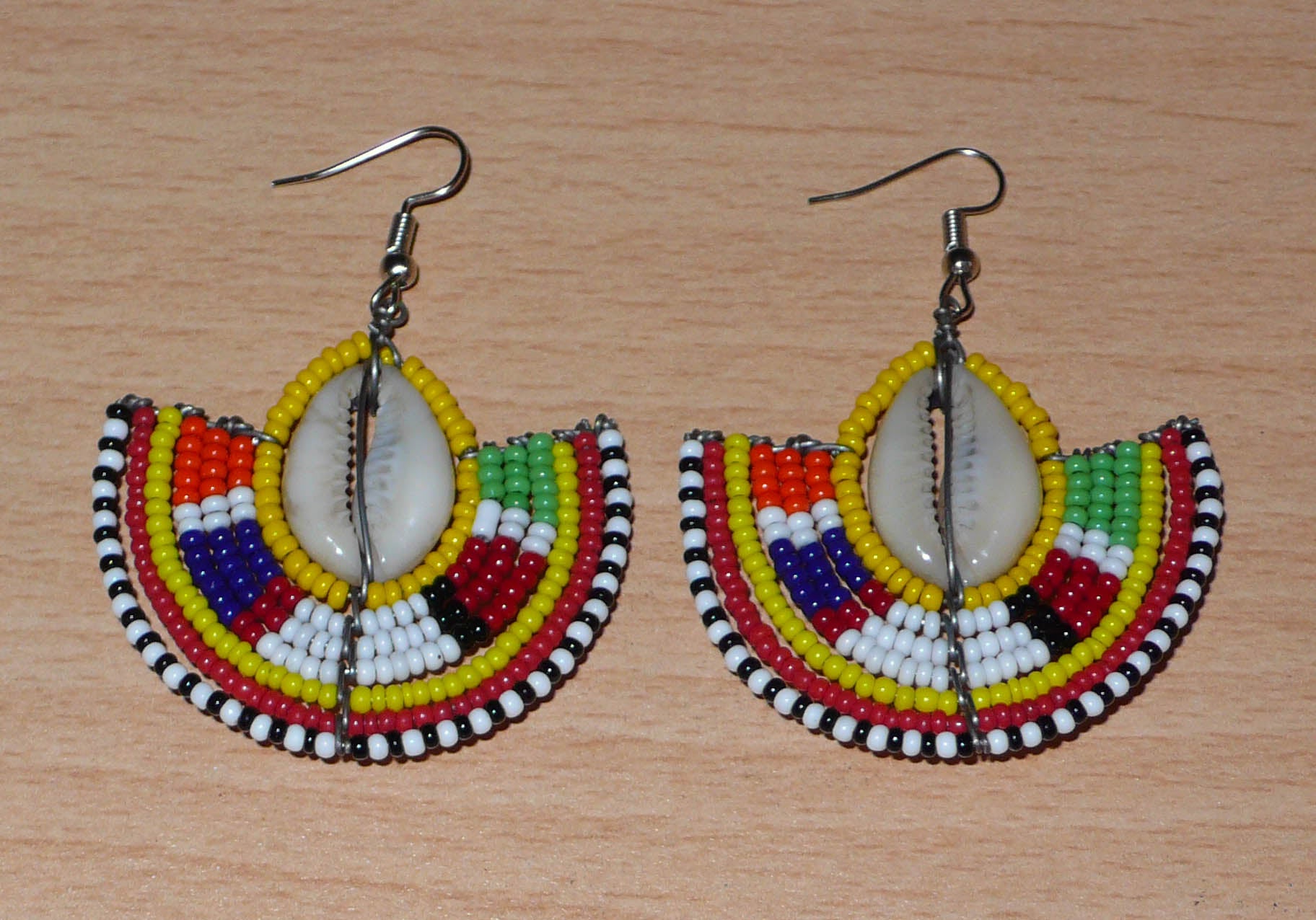 Ces jolies boucles d'oreilles à l'allure ethnique afro chic se composent de perles de rocaille jaunes et multicolores et de coquillages cauris. De taille moyenne, elles mesurent 6 cm de long et 4.5 cm de large, et se portent avec des crochets en acier inoxydable sur des oreilles percées.
