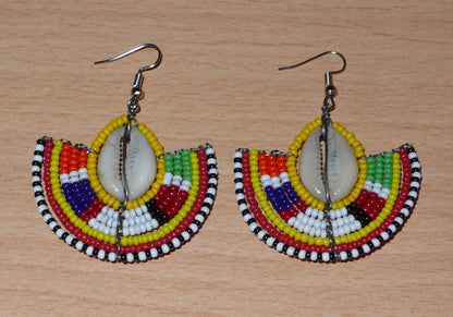 Ces jolies boucles d'oreilles à l'allure ethnique afro chic se composent de perles de rocaille jaunes et multicolores et de coquillages cauris. De taille moyenne, elles mesurent 6 cm de long et 4.5 cm de large, et se portent avec des crochets en acier inoxydable sur des oreilles percées.