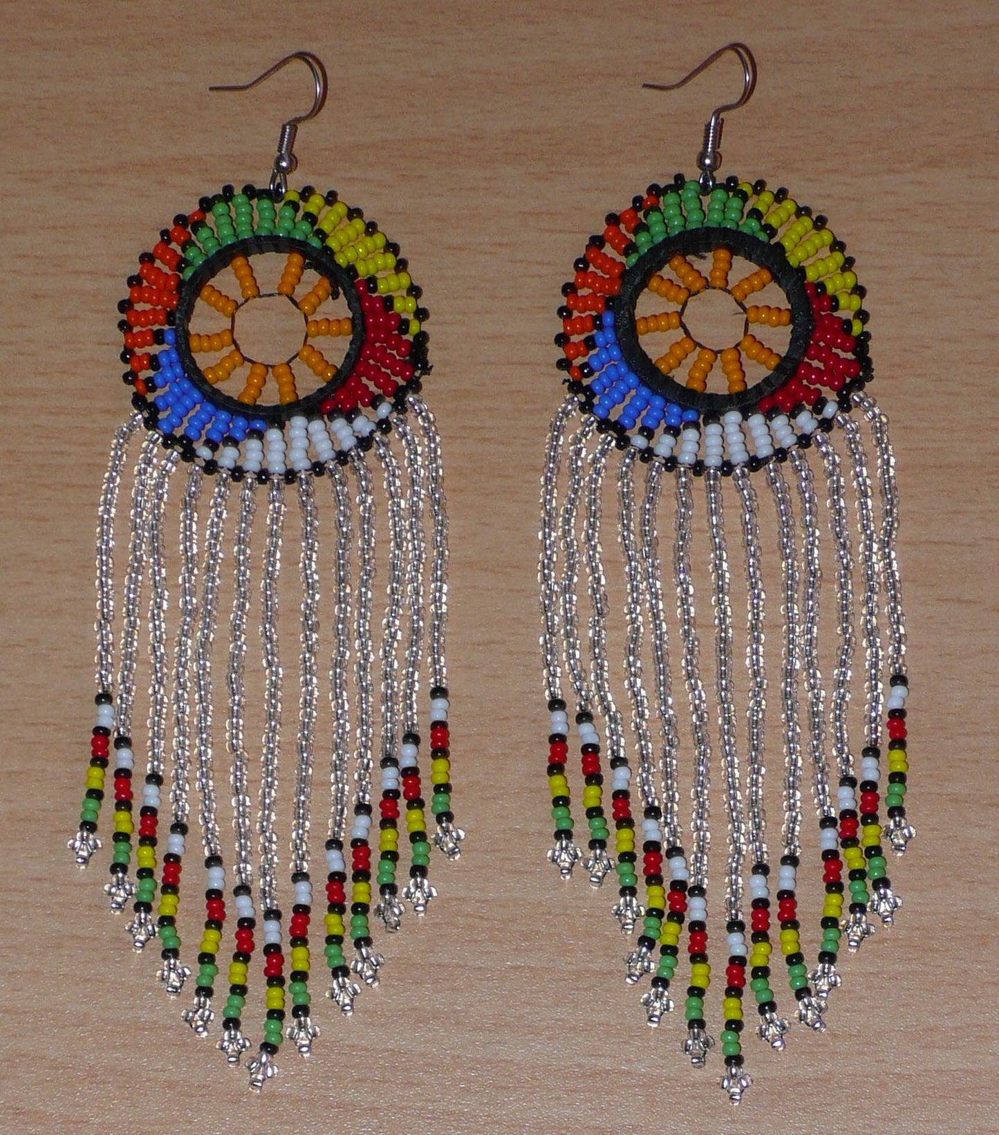 Longues boucles d'oreilles sud-africaines traditionnelles à franges et motifs zoulous composées de perles de rocaille gris clair translucides et multicolores. Elles mesurent 14,5 cm de long et 4,5 cm de large, et elles se portent avec des crochets en acier inoxydable sur des oreilles percées.