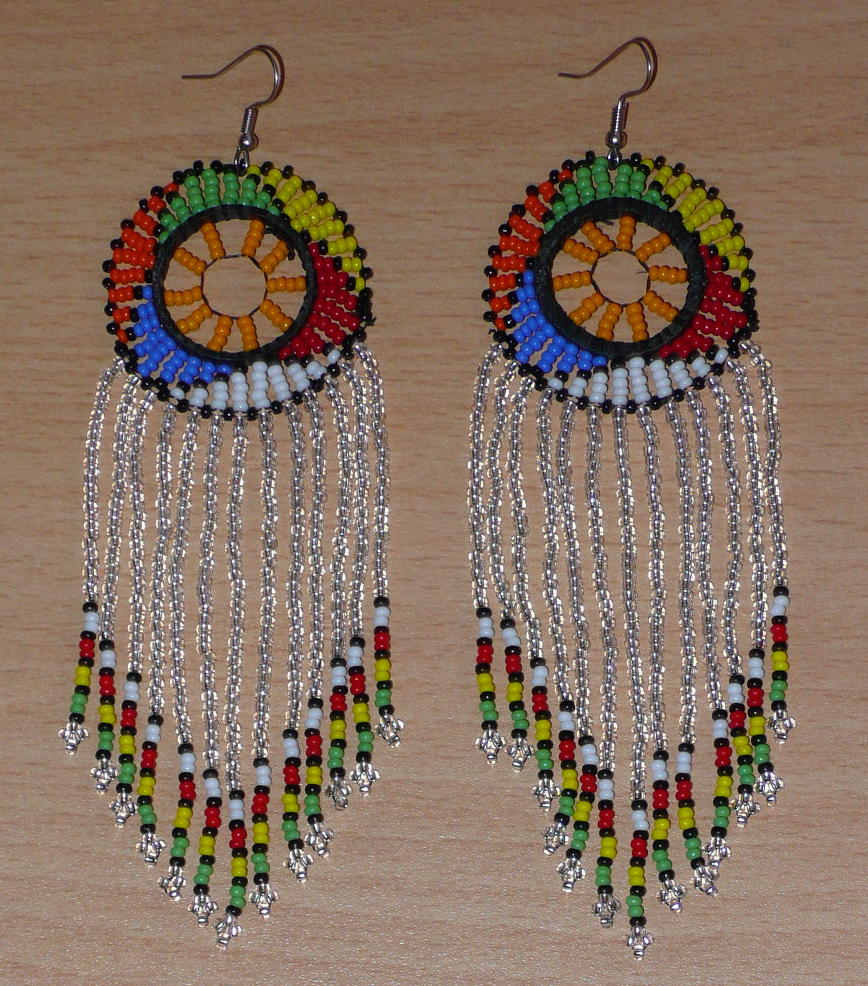 Longues boucles d'oreilles sud-africaines traditionnelles à franges et motifs zoulous composées de perles de rocaille gris clair translucides et multicolores. Elles mesurent 14,5 cm de long et 4,5 cm de large, et elles se portent avec des crochets en acier inoxydable sur des oreilles percées.