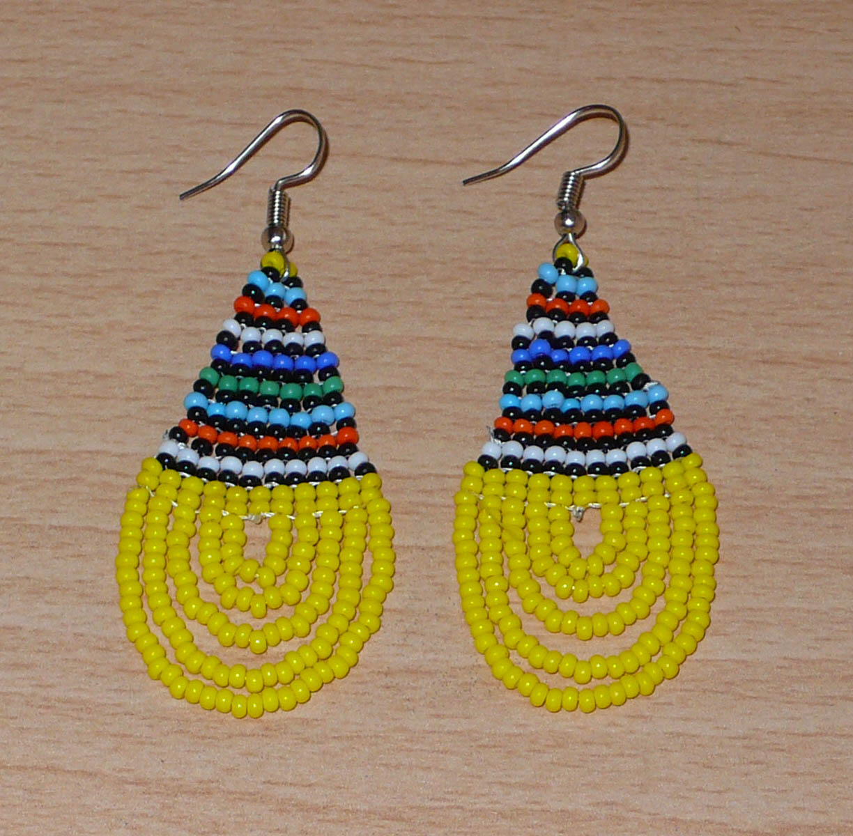 Boucles d'oreilles africaines traditionnelles zouloues en forme de gouttes composées d'un tissage de perles de rocaille jaunes et multicolores. Elles mesurent 7 cm de long et 2,5 cm de large et se portent sur des oreilles percées.