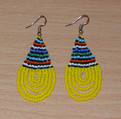 Boucles d'oreilles africaines traditionnelles zouloues en forme de gouttes composées d'un tissage de perles de rocaille jaunes et multicolores. Elles mesurent 7 cm de long et 2,5 cm de large et se portent sur des oreilles percées.