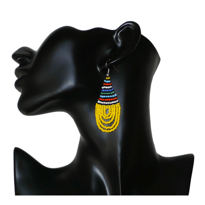 Boucles d'oreilles africaines traditionnelles zouloues en forme de gouttes composées d'un tissage de perles de rocaille jaunes et multicolores. Elles mesurent 7 cm de long et 2,5 cm de large et se portent sur des oreilles percées.