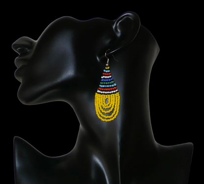 Boucles d'oreilles africaines traditionnelles zouloues en forme de gouttes composées d'un tissage de perles de rocaille jaunes et multicolores. Elles mesurent 7 cm de long et 2,5 cm de large et se portent sur des oreilles percées.
