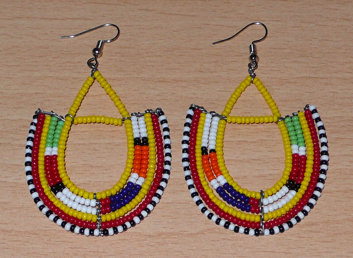 Boucles d'oreilles africaines traditionnelles à motifs ethniques Massai composées de perles jaunes et multicolores montées en forme d'ancres . Elles mesurent 7,5 cm de long et 4,5 cm de large et se portent avec des crochets en acier inoxydable sur des oreilles percées.