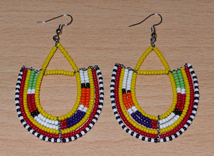 Boucles d'oreilles africaines traditionnelles à motifs ethniques Massai composées de perles jaunes et multicolores montées en forme d'ancres . Elles mesurent 7,5 cm de long et 4,5 cm de large et se portent avec des crochets en acier inoxydable sur des oreilles percées.