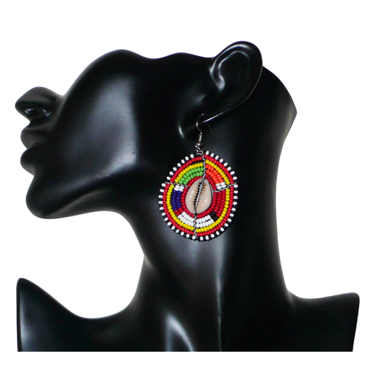Boucles d'oreilles africaines traditionnelles en forme de boucliers Massai composées de perles de rocaille rouges et multicolores et de coquillages. De taille moyenne, elles mesurent 6 cm de long et 4 cm de large, et se portent avec des crochets en acier inoxydable sur des oreilles percées.