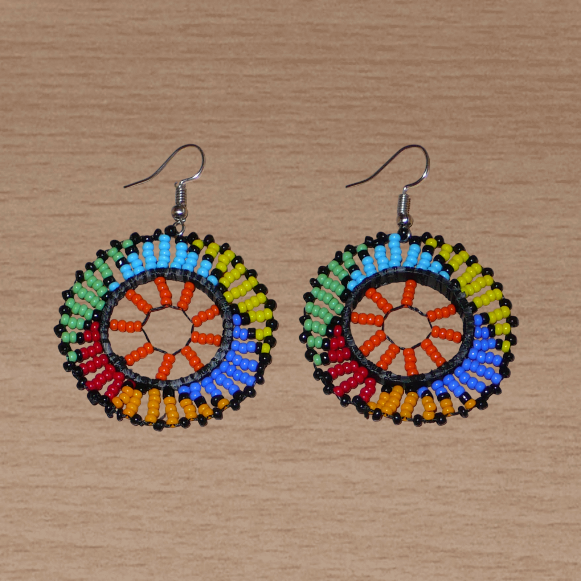 Boucles d'oreilles africaines rondes à motifs ethniques zoulous composées de perles de rocaille orange et multicolores glissées sur des fils de nylon fixés sur des structures circulaires en plastique. Elles mesurent 6 cm de long et 4 cm de large et se portent sur des oreilles percées. 