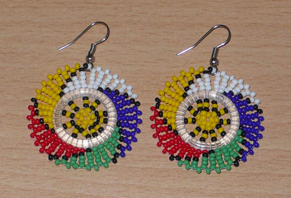 Boucles d'oreilles sud-africaines rondes à motifs traditionnels zoulous composées de perles de rocaille multicolores. Elles mesurent 5.5 cm de long et 4 cm de large, et se portent sur des oreilles percées.