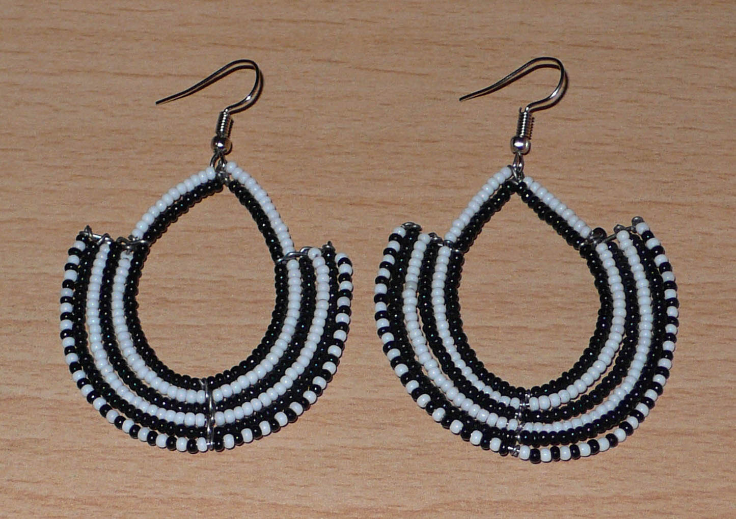 Boucles d'oreilles ethniques bicolores composées de perles de rocaille noires et blanches glissées sur des structures en fils de fer montés en forme d'ancres. Elles mesurent 7 cm de long et 4,5 cm de large et se portent sur des oreilles percées.
