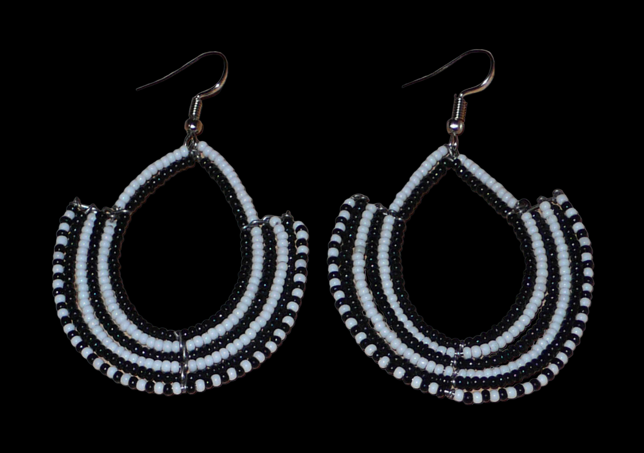 Boucles d'oreilles ethniques bicolores composées de perles de rocaille noires et blanches glissées sur des structures en fils de fer montés en forme d'ancres. Elles mesurent 7 cm de long et 4,5 cm de large et se portent sur des oreilles percées.