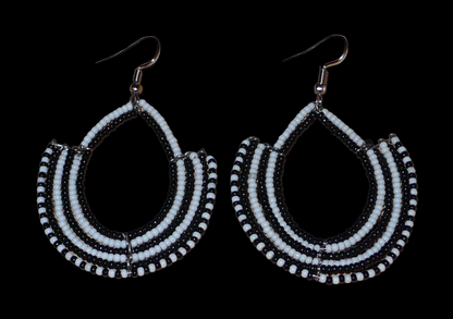 Boucles d'oreilles ethniques bicolores composées de perles de rocaille noires et blanches glissées sur des structures en fils de fer montés en forme d'ancres. Elles mesurent 7 cm de long et 4,5 cm de large et se portent sur des oreilles percées.