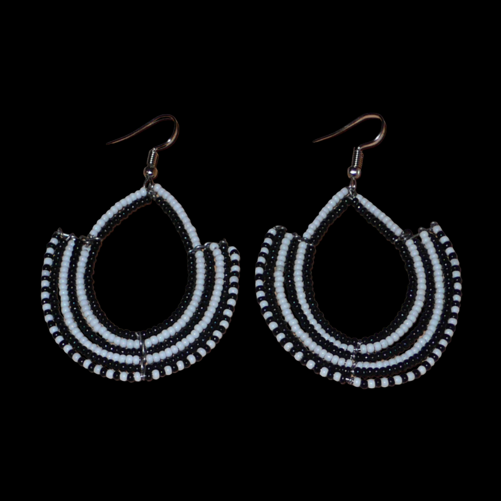 Boucles d'oreilles ethniques bicolores composées de perles de rocaille noires et blanches glissées sur des structures en fils de fer montés en forme d'ancres. Elles mesurent 7 cm de long et 4,5 cm de large et se portent sur des oreilles percées.