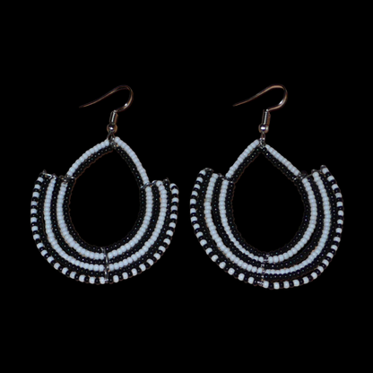 Boucles d'oreilles ethniques bicolores composées de perles de rocaille noires et blanches glissées sur des structures en fils de fer montés en forme d'ancres. Elles mesurent 7 cm de long et 4,5 cm de large et se portent sur des oreilles percées.