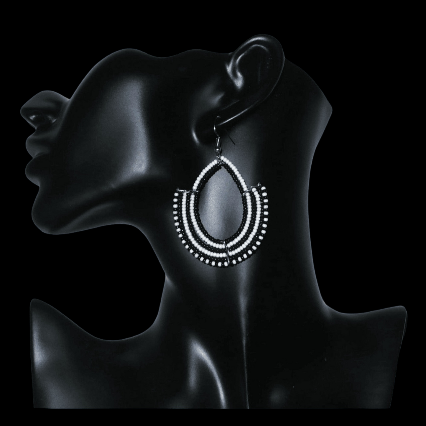 Boucles d'oreilles ethniques bicolores composées de perles de rocaille noires et blanches glissées sur des structures en fils de fer montés en forme d'ancres. Elles mesurent 7 cm de long et 4,5 cm de large et se portent sur des oreilles percées.