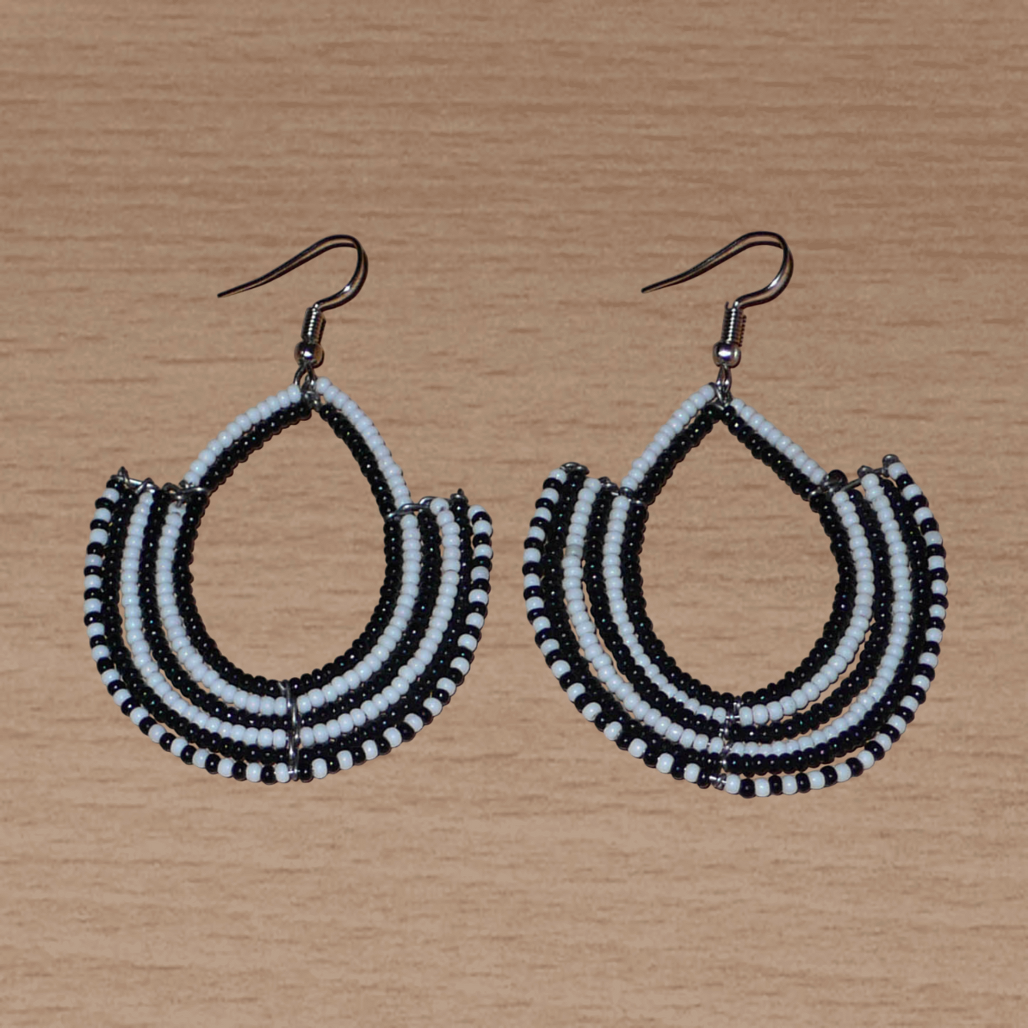 Boucles d'oreilles ethniques bicolores composées de perles de rocaille noires et blanches glissées sur des structures en fils de fer montés en forme d'ancres. Elles mesurent 7 cm de long et 4,5 cm de large et se portent sur des oreilles percées.