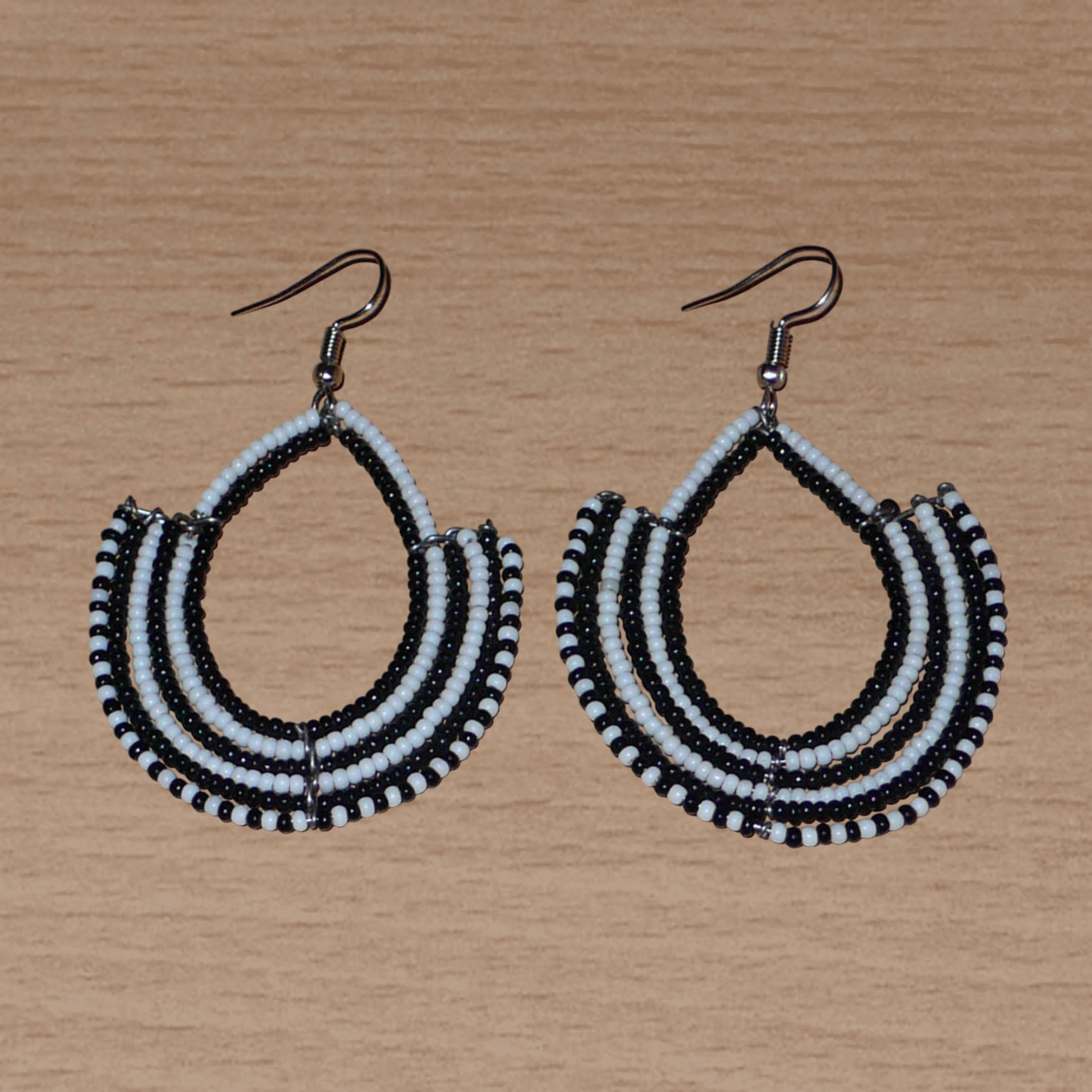 Boucles d'oreilles ethniques bicolores composées de perles de rocaille noires et blanches glissées sur des structures en fils de fer montés en forme d'ancres. Elles mesurent 7 cm de long et 4,5 cm de large et se portent sur des oreilles percées.
