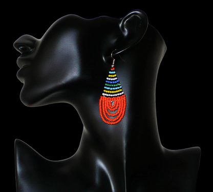 Boucles d'oreilles africaines en forme de gouttes faites de perles de rocaille orange et multicolores. Elles mesurent 7 cm de long et 2,5 cm de large, et se portent sur des oreilles percées.