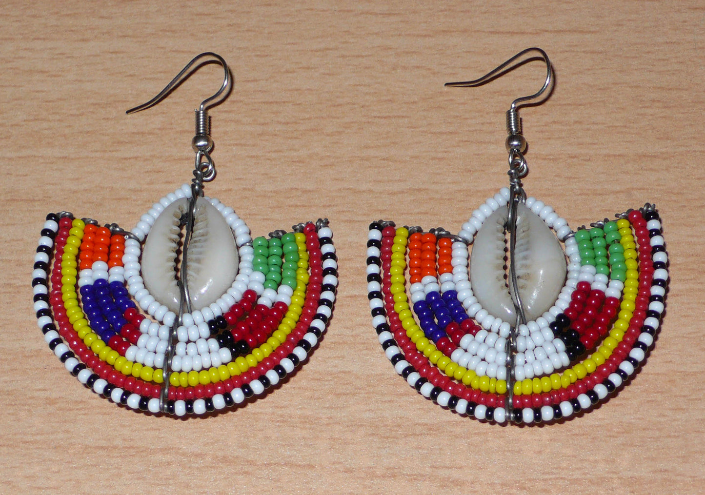 Apportez une touche de couleur et d'authenticité à votre style avec cette paire de boucles d'oreilles africaines issues de l'artisanat traditionnel Massai. Confectionnées à la main au Kenya, ces boucles d'oreilles ethniques se composent de perles de rocaille blanches et multicolores et de coquillages cauris. De taille moyenne, elles mesurent 6 cm de long et 4.5 cm de large, et se portent avec des crochets en acier inoxydable sur des oreilles percées.