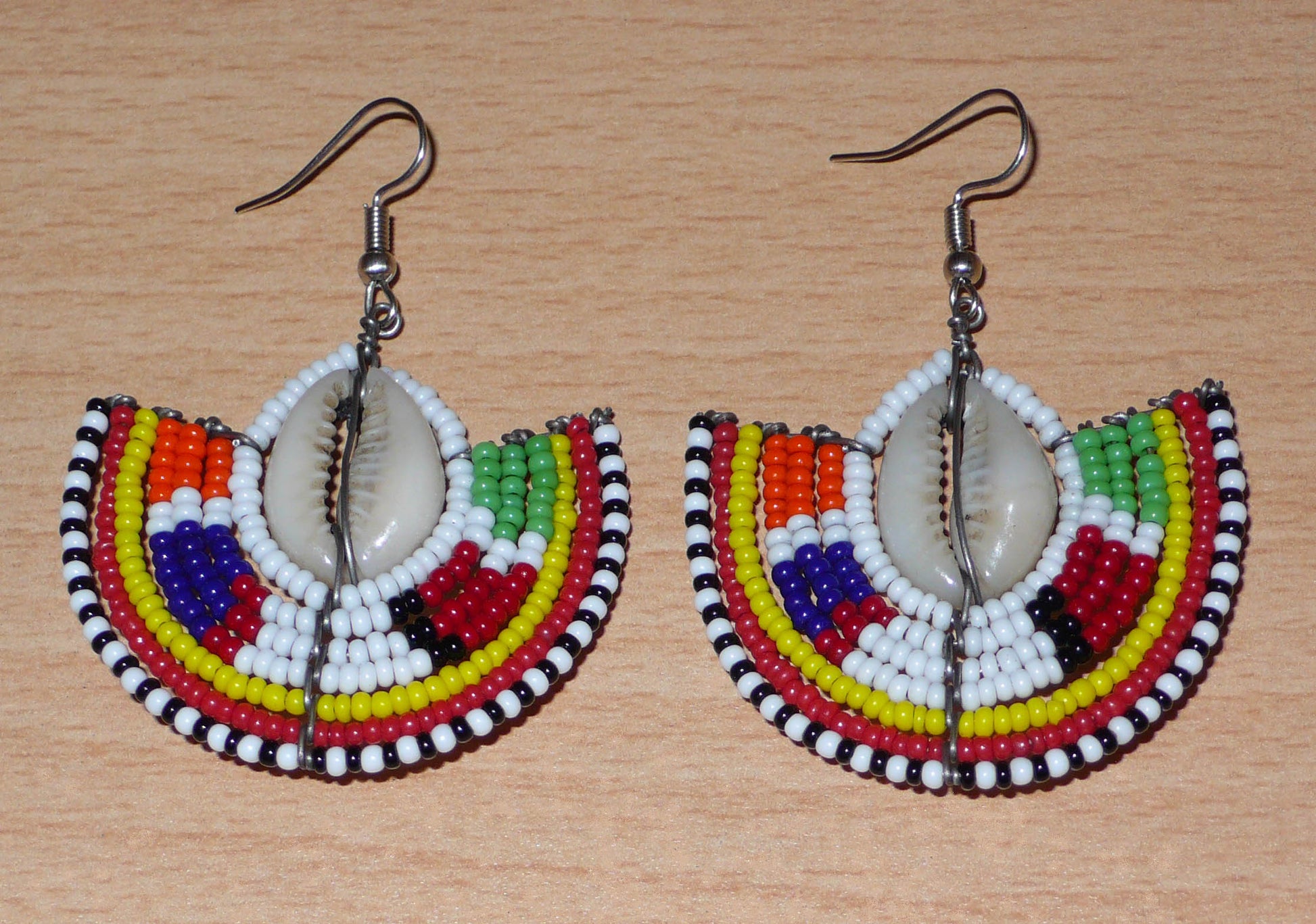 Apportez une touche de couleur et d'authenticité à votre style avec cette paire de boucles d'oreilles africaines issues de l'artisanat traditionnel Massai. Confectionnées à la main au Kenya, ces boucles d'oreilles ethniques se composent de perles de rocaille blanches et multicolores et de coquillages cauris. De taille moyenne, elles mesurent 6 cm de long et 4.5 cm de large, et se portent avec des crochets en acier inoxydable sur des oreilles percées.