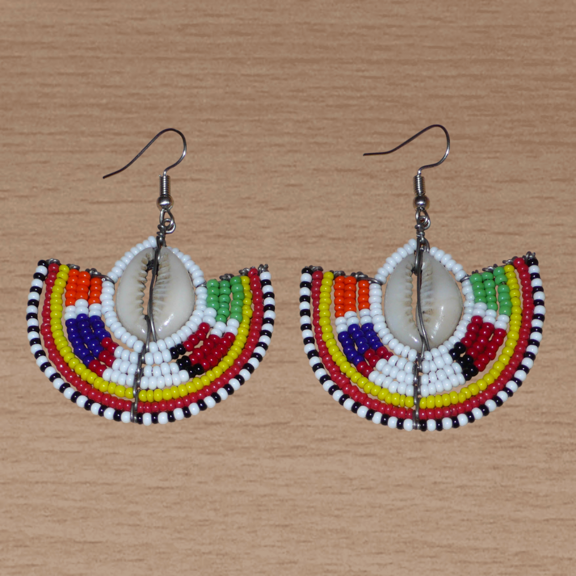 Apportez une touche de couleur et d'authenticité à votre style avec cette paire de boucles d'oreilles africaines issues de l'artisanat traditionnel Massai. Confectionnées à la main au Kenya, ces boucles d'oreilles ethniques se composent de perles de rocaille blanches et multicolores et de coquillages cauris. De taille moyenne, elles mesurent 6 cm de long et 4.5 cm de large, et se portent avec des crochets en acier inoxydable sur des oreilles percées.