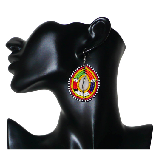 Ambiance exotique avec ces jolies boucles d'oreilles africaines à motifs ethniques traditionnels Massai de conception artisanale kenyane. Elles sont composées de perles de rocaille jaunes et multicolores et de coquillages cauris fixés sur des fils de fer montés en forme de boucliers Massai. Ces boucles d'oreilles de taille moyenne mesurent 6.5 cm de long et 4 cm de large ; elles se portent avec des crochets en acier inoxydable sur des oreilles percées.
