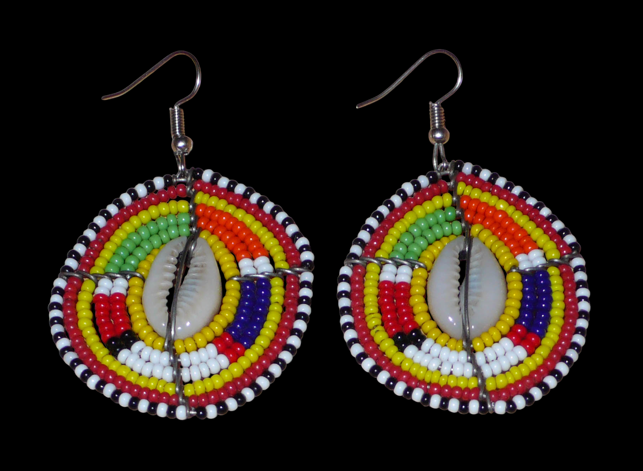 Ambiance exotique avec ces jolies boucles d'oreilles africaines à motifs ethniques traditionnels Massai de conception artisanale kenyane. Elles sont composées de perles de rocaille jaunes et multicolores et de coquillages cauris fixés sur des fils de fer montés en forme de boucliers Massai. Ces boucles d'oreilles de taille moyenne mesurent 6.5 cm de long et 4 cm de large ; elles se portent avec des crochets en acier inoxydable sur des oreilles percées.