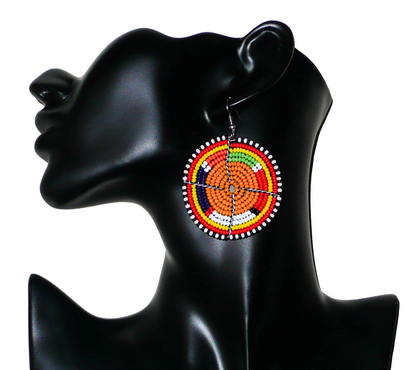 Boucles d'oreilles africaines de tradition Massai composées de perles de rocaille orange et multicolores enfilées sur des structures circulaires en fils de fer. De taille moyenne, elles mesurent 6,5 cm de long et 4,5 cm de large ; elle se portent sur des oreilles percées. Présentées sur un mannequin. Timeless Fineries
