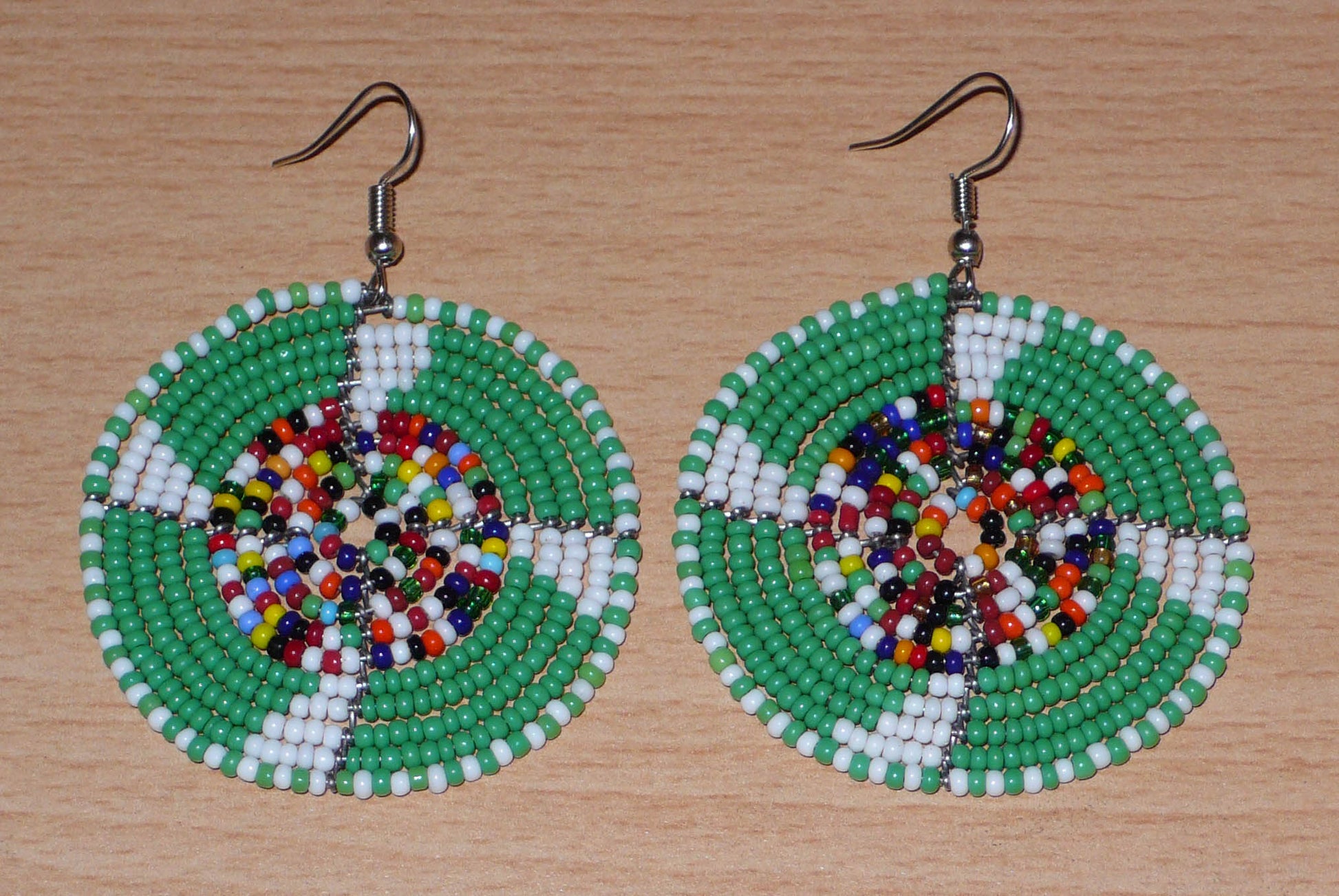 Ajoutez une touche ethnique afro bohème à votre look avec ces boucles d'oreilles africaines rondes confectionnées à la main dans la tradition artisanale Massai : elles se composent de perles de rocaille principalement vertes, puis blanches et multicolores glissées sur des structures circulaires en fils de fer.
Cette paire de boucles d'oreilles mesure 6.5 cm de long et 4.5 cm de large, et se porte avec des crochets en acier inoxydable sur des oreilles percées.