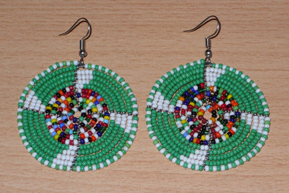 Ajoutez une touche ethnique afro bohème à votre look avec ces boucles d'oreilles africaines rondes confectionnées à la main dans la tradition artisanale Massai : elles se composent de perles de rocaille principalement vertes, puis blanches et multicolores glissées sur des structures circulaires en fils de fer.
Cette paire de boucles d'oreilles mesure 6.5 cm de long et 4.5 cm de large, et se porte avec des crochets en acier inoxydable sur des oreilles percées.
