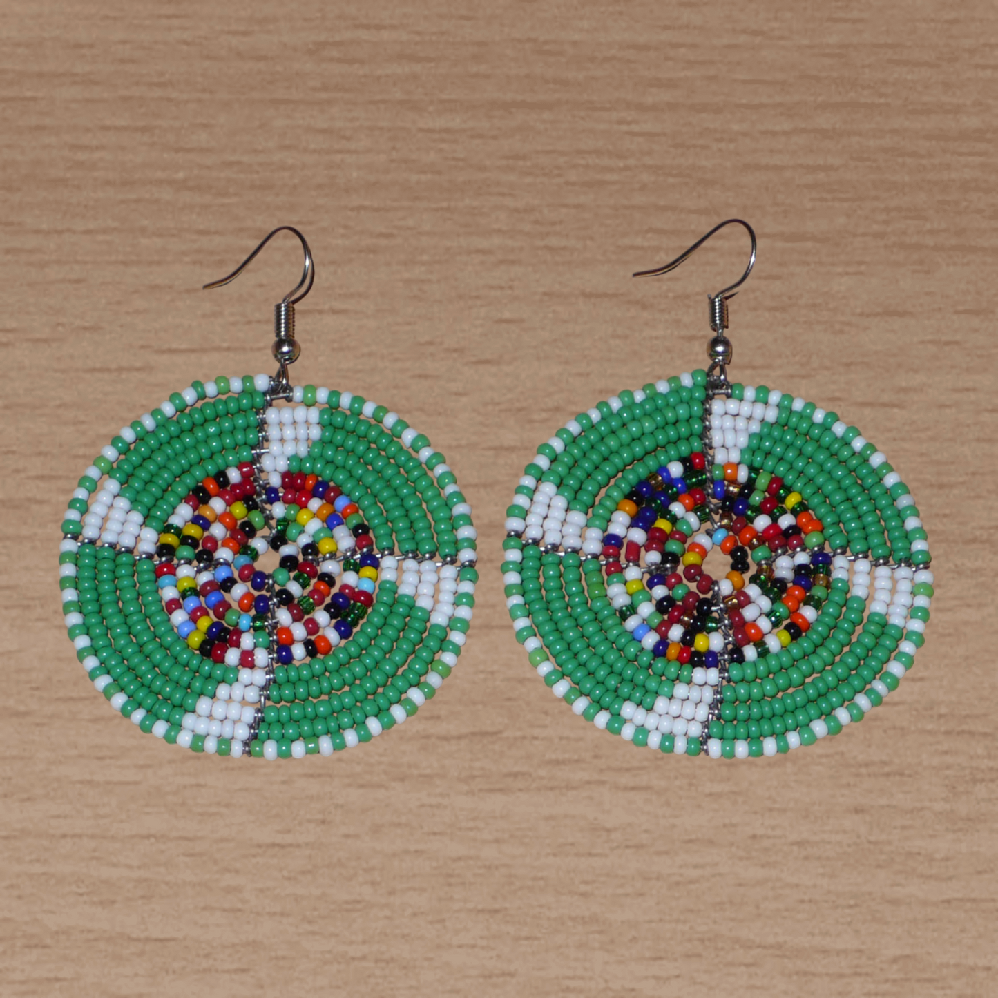 Ajoutez une touche ethnique afro bohème à votre look avec ces boucles d'oreilles africaines rondes confectionnées à la main dans la tradition artisanale Massai : elles se composent de perles de rocaille principalement vertes, puis blanches et multicolores glissées sur des structures circulaires en fils de fer.
Cette paire de boucles d'oreilles mesure 6.5 cm de long et 4.5 cm de large, et se porte avec des crochets en acier inoxydable sur des oreilles percées.
