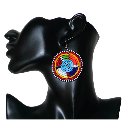 Boucles d'oreilles africaines bleues et multicolores à motifs ethniques traditionnels Massai, composées d'un tissage de perles de rocaille glissées sur des structures circulaires en fils de fer. De taille moyenne, ces boucles d'oreilles perlées mesurent 6.5 cm de long et 4.5 cm de large et se portent avec des crochets en acier inoxydable sur des oreilles percées.