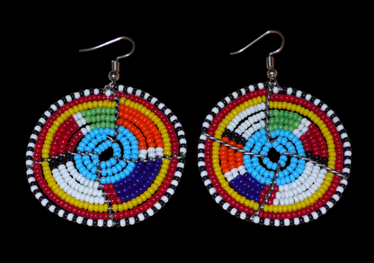 Boucles d'oreilles africaines bleues et multicolores à motifs ethniques traditionnels Massai, composées d'un tissage de perles de rocaille glissées sur des structures circulaires en fils de fer. De taille moyenne, ces boucles d'oreilles perlées mesurent 6.5 cm de long et 4.5 cm de large et se portent avec des crochets en acier inoxydable sur des oreilles percées.