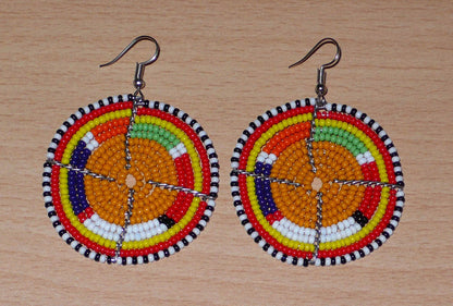 Boucles d'oreilles africaines Massai rondes fabriquées au Kenya, faites de perles de rocaille orange et multicolores. De taille moyenne, ces boucles d'oreilles mesurent 6,5 cm de long et 4,5 cm de large ; elles se portent avec des crochets en acier inoxydable sur des oreilles percées.