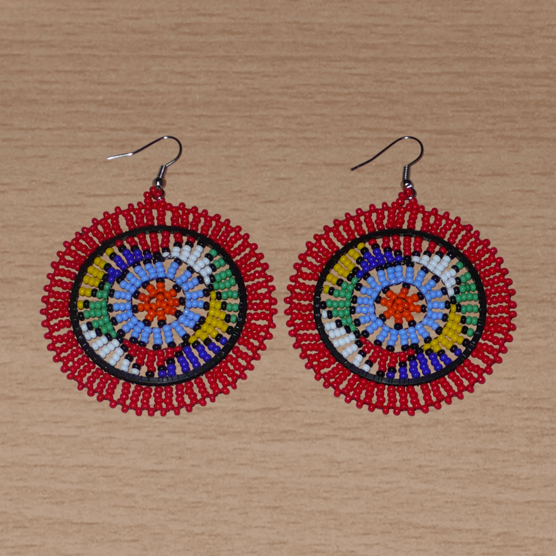 Boucles d'oreilles africaines à motifs zoulous composées de perles de rocailles rouges et multicolores enfilées sur des structures circulaires en fils de fer et de nylon.