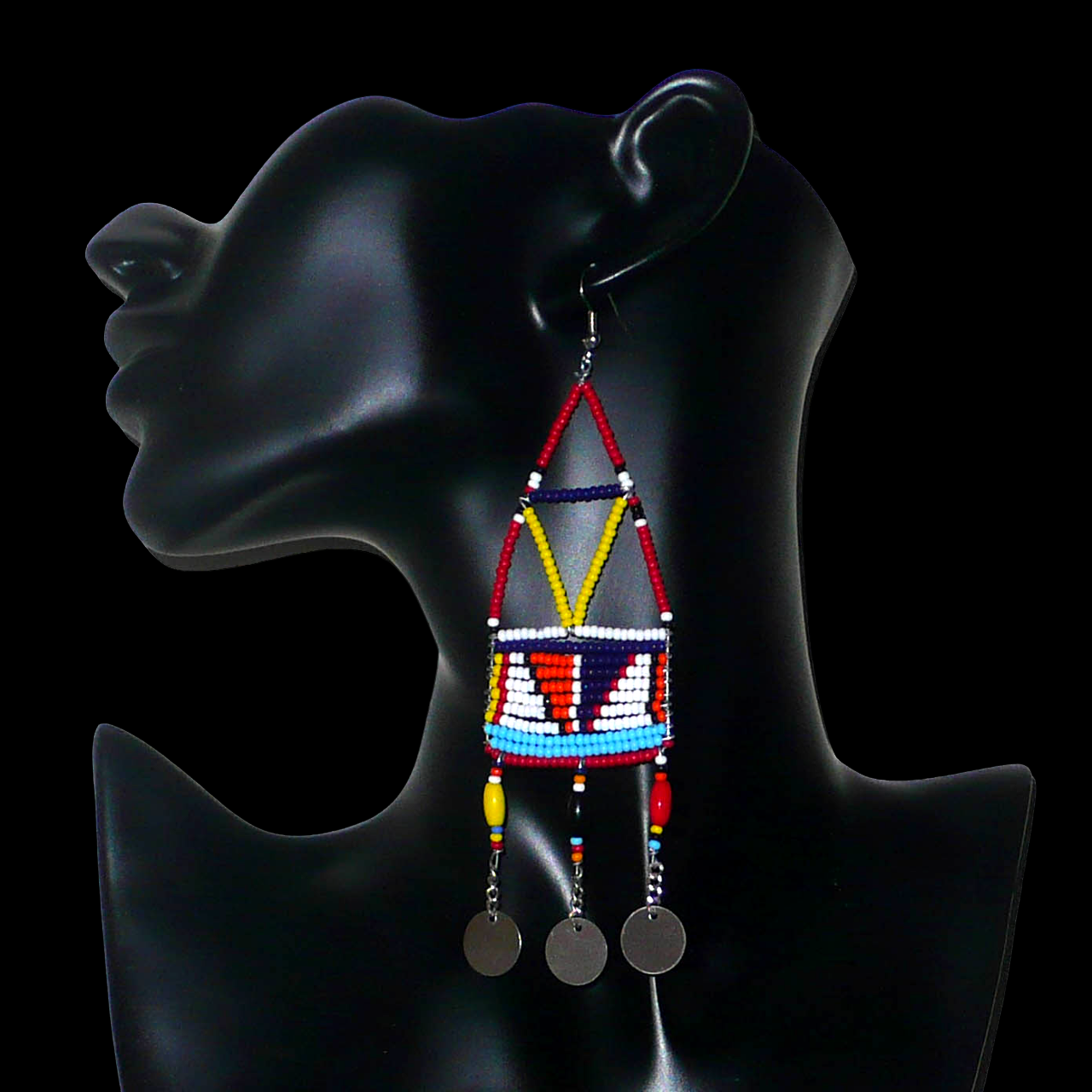 Bijoux africains. Longues boucles d'oreilles africaines de tradition Massai. Mesurant 13 cm de long et 4 cm de large, elles se composent de perles de rocaille et de plastique rouges et multicolores enfilées sur des trames géométriques en fils de fer. Elles se prolongent de trois chainettes perlées se terminant par trois pastilles en métal. Elles se portent sur des oreilles percées, avec des crochets en acier inoxydable. Présentées sur un mannequin. Timeless Fineries