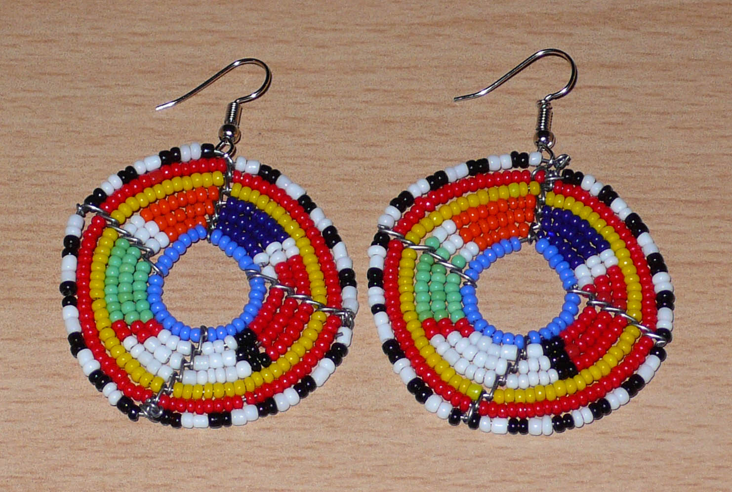 Boucles d'oreilles africaines Massai en perles de rocaille multicolores enfilées sur des structures circulaires en fils de fer. Elles mesurent 6,5 cm de long et 4,5 cm de large.