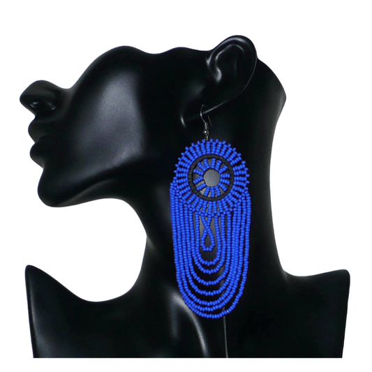 Longues boucles d'oreilles sud-africaines à franges perlées : de tradition artisanale zouloue, elles se composent d'un tissage de perles de rocaille bleues enfilées sur des fils de nylon fixés à un cercle de plastique noir. Cette paire de boucles d'oreilles aux accents ethniques mesure 12 cm de long et 4.5 cm de large et se porte avec des crochets en acier inoxydable sur des oreilles percées.