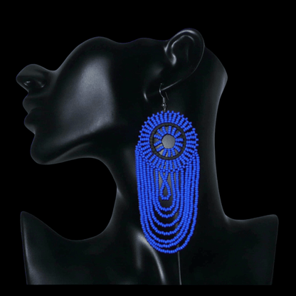 Longues boucles d'oreilles sud-africaines à franges perlées : de tradition artisanale zouloue, elles se composent d'un tissage de perles de rocaille bleues enfilées sur des fils de nylon fixés à un cercle de plastique noir. Cette paire de boucles d'oreilles aux accents ethniques mesure 12 cm de long et 4.5 cm de large et se porte avec des crochets en acier inoxydable sur des oreilles percées.