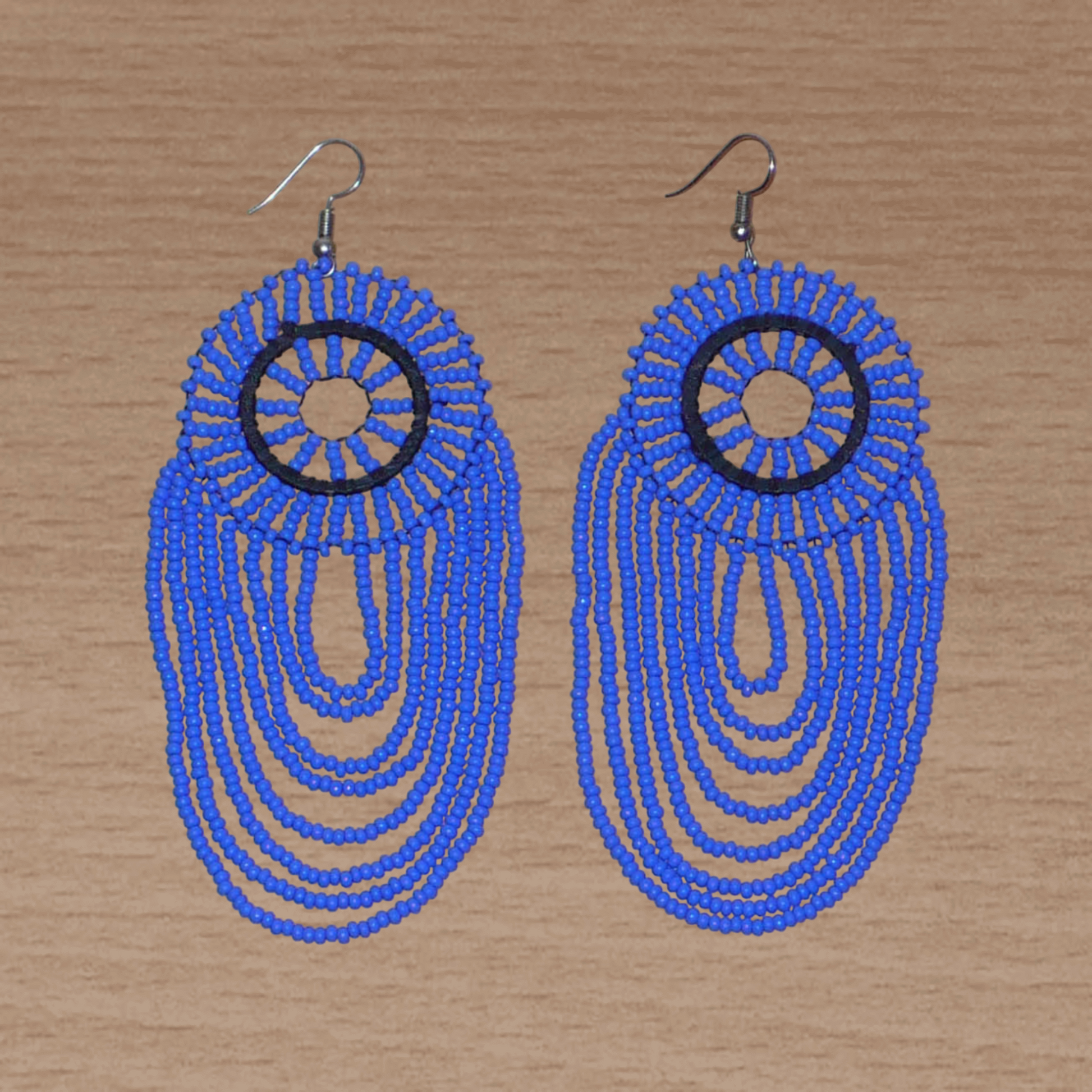 Longues boucles d'oreilles sud-africaines à franges perlées : de tradition artisanale zouloue, elles se composent d'un tissage de perles de rocaille bleues enfilées sur des fils de nylon fixés à un cercle de plastique noir. Cette paire de boucles d'oreilles aux accents ethniques mesure 12 cm de long et 4.5 cm de large et se porte avec des crochets en acier inoxydable sur des oreilles percées.