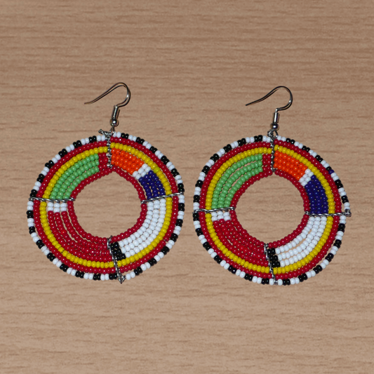 Boucles d'oreilles africaines rondes aux motifs et couleurs Massai composées de perles de rocaille rouges et multicolores enfilées sur sept rangées de fils de fer montés en forme de cercles. Elles mesurent 7,5 cm de long et 5,5 cm de large et se portent avec des crochets en acier inoxydable sur des oreilles percées.