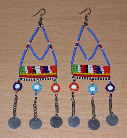 Boucles d'oreilles africaines Massai composées de perles de rocaille bleues et multicolores et de perles en plastique enfilées sur des structures à formes géométriques en fils de fer, et se prolongent de chaînettes décorées de disques métalliques. Surdimensionnées, elles mesurent 14.5 cm de long et se portent sur des oreilles percées.