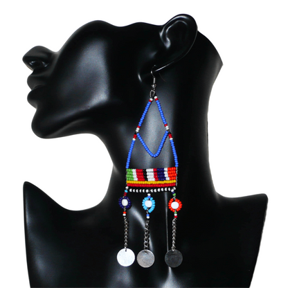 Boucles d'oreilles africaines Massai composées de perles de rocaille bleues et multicolores et de perles en plastique enfilées sur des structures à formes géométriques en fils de fer, et se prolongent de chaînettes décorées de disques métalliques. Surdimensionnées, elles mesurent 14.5 cm de long et se portent sur des oreilles percées.