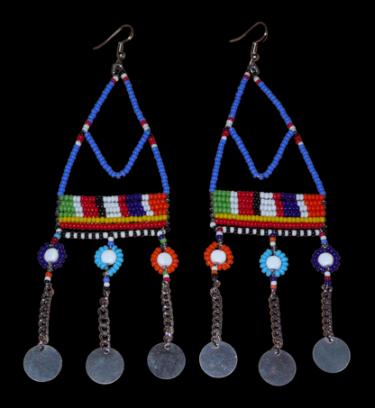 Boucles d'oreilles africaines Massai composées de perles de rocaille bleues et multicolores et de perles en plastique enfilées sur des structures à formes géométriques en fils de fer, et se prolongent de chaînettes décorées de disques métalliques. Surdimensionnées, elles mesurent 14.5 cm de long et se portent sur des oreilles percées.